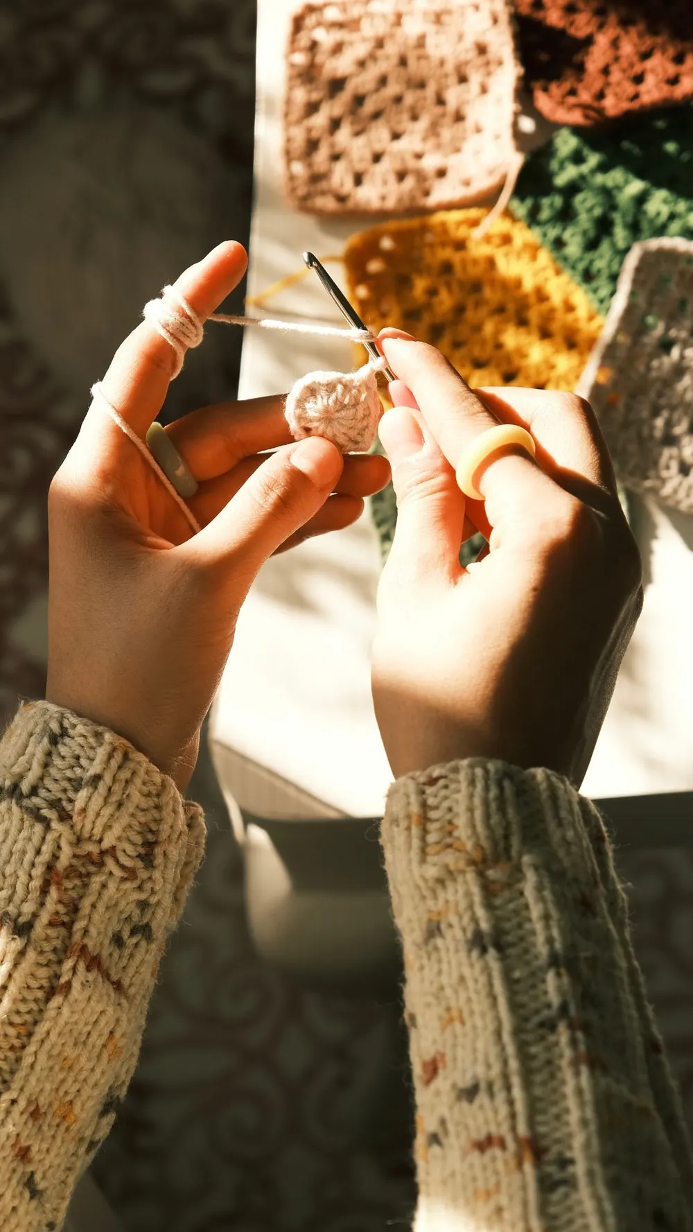 Hands crocheting granny squares in warm sunlight
